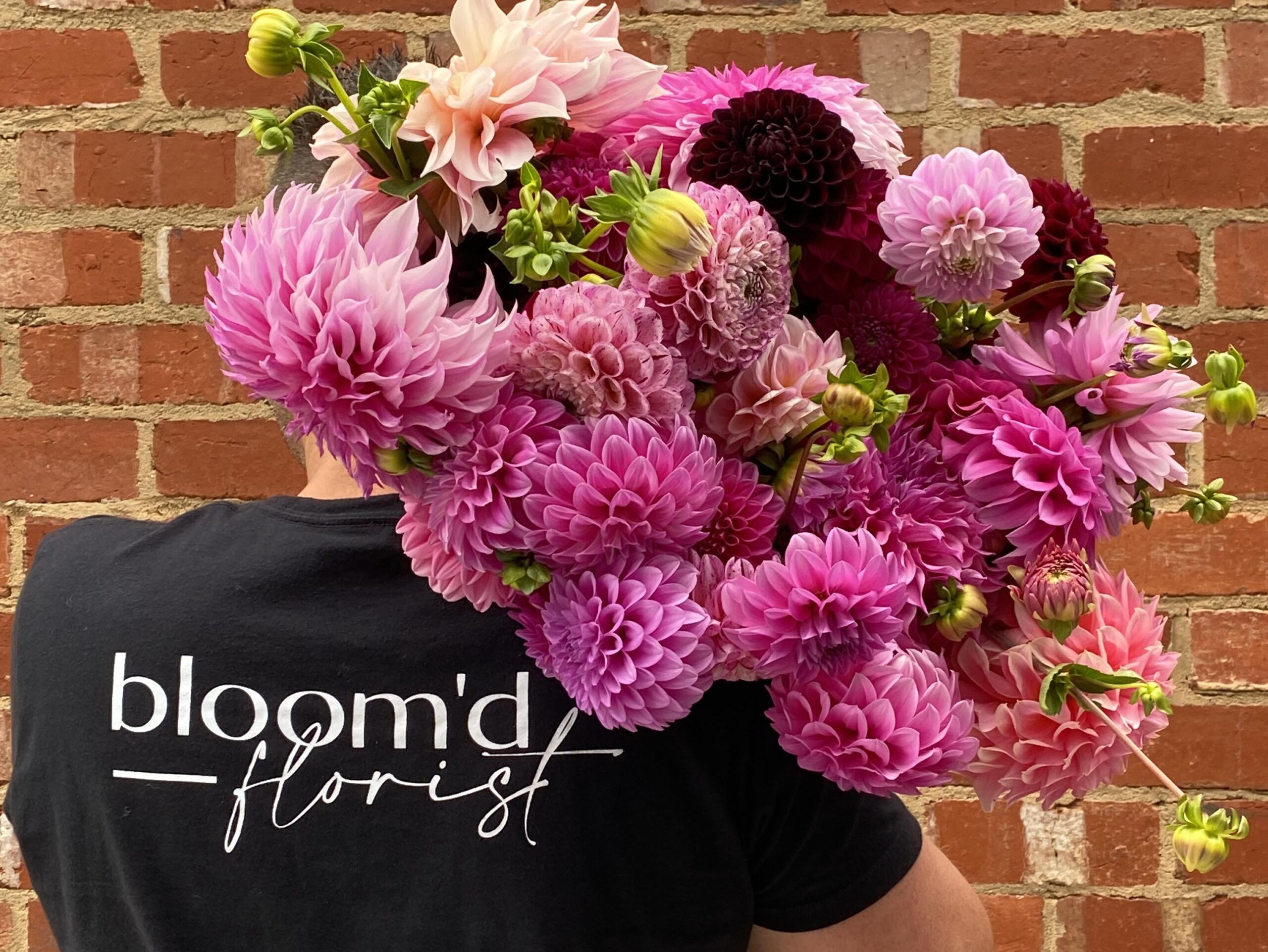 A Man Wearing A Bloom'd Florist T-Shirt Carries A Bunch Of Pink & Green Flowers